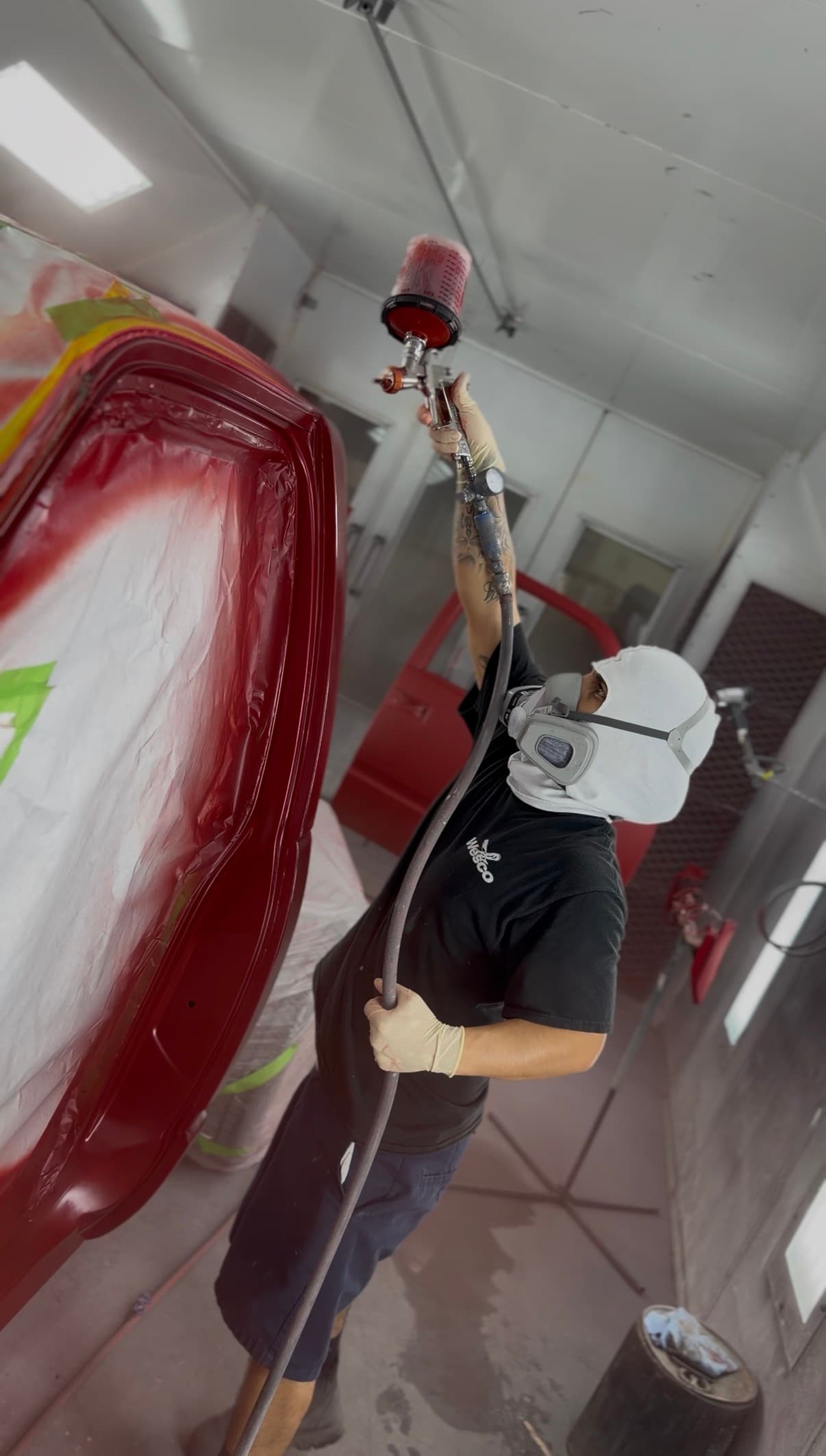 Painter spraying a red vehicle panel in the paint booth
